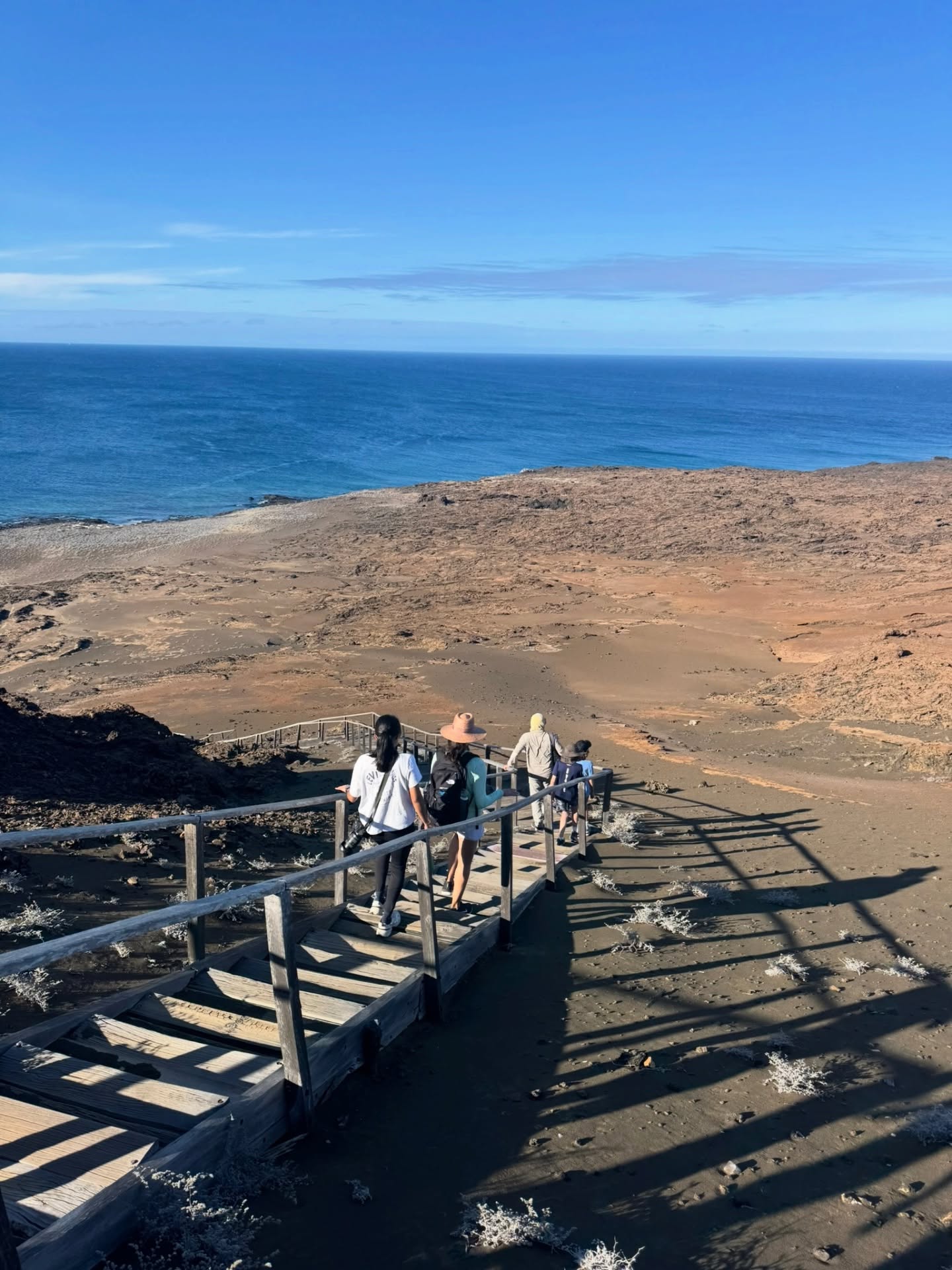 Group walking along wooden boardwalk toward ocean in Galapagos coastal landscape | Ile Tours