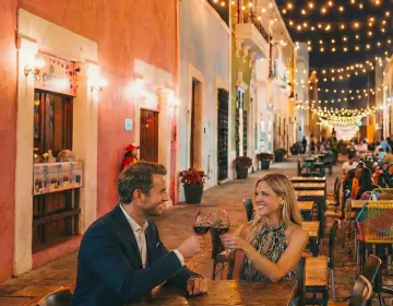 Stylish couple dining al fresco on the cobblestone street Calle 59 in Campeche surrounded by pastel colonial houses | Ile Tours