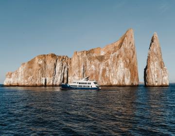 Cruise ship floating near twin vertical rock formation in Galapagos | Ile Tours