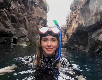 Person snorkeling between volcanic cliffs in Galapagos clear waters | Ile Tours