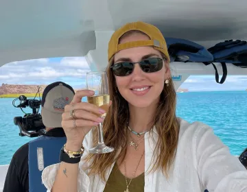 Traveler holding champagne glass on Galapagos yacht with volcanic island scenery | Ile Tours