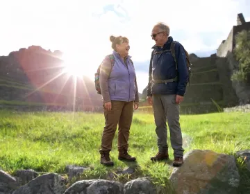 Senior travelers exploring archaeological ruins with backpacks and lens flare sunlight | Ile Tours