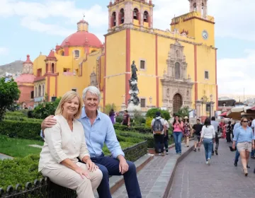 Senior travelers seated in colonial plaza with ornate yellow church and landscaped pathways | Ile Tours