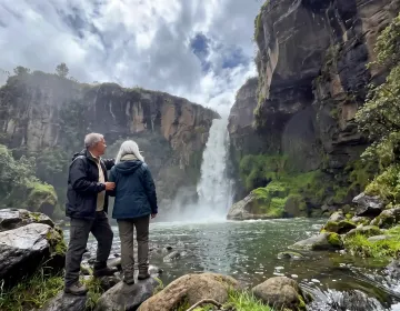 Senior couple standing near waterfall surrounded by Andean mountains and cloud forest scenery in Ecuador