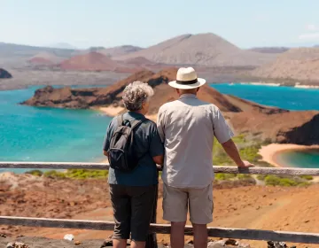 Senior couple standing at Bartolomé Island viewpoint overlooking Pinnacle Rock, volcanic landscapes, and turquoise waters in the Galápagos Islands