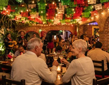 Senior couple celebrating with wine during private romantic dinner in Mexican courtyard restaurant with live mariachi music | Ile Tours