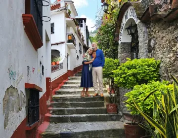 Senior travelers embracing in colonial alleyway with hotel sign and greenery | Ile Tours