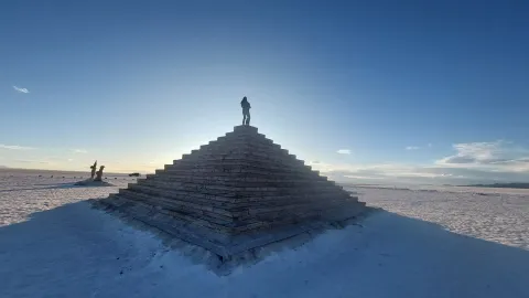 Discover Unique Landmarks on Your Journey with Ile Tours Silhouette of a person standing atop a pyramid structure against a vast, open sky at sunset | Ile Tours