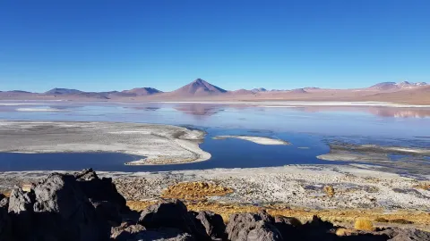 Explore the Stunning Salar de Uyuni | Ile Tours A breathtaking view of a vast salt flat with a serene lake reflecting the blue sky and mountains in the background. | Ile Tours