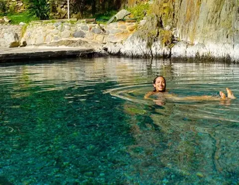Una nadadora alegre relajándose en las aguas cristalinas de una piscina natural rodeada de acantilados rocosos | Ile Tours