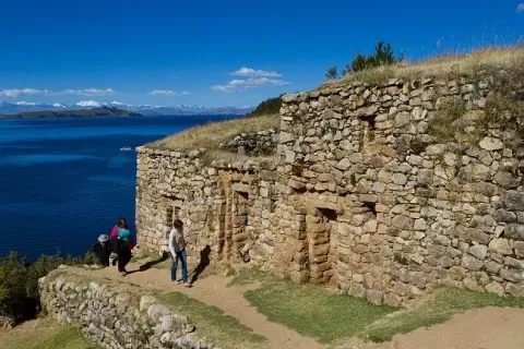 Uncover Ancient Mysteries on Your Adventure with Ile Tours Tourists exploring ancient stone ruins overlooking a serene body of water and distant mountains under a clear blue sky | Ile Tours