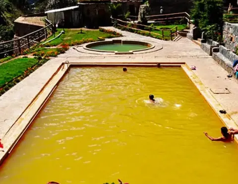 Visitors enjoying a natural mineral pool with vibrant yellow water, surrounded by lush gardens and scenic views | Ile Tours