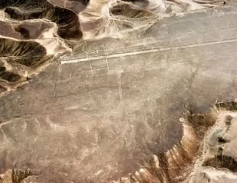 Vista aérea de las Líneas de Nazca con el geoglifo del Colibrí grabado en el desierto peruano, rodeado de terreno árido y cordones montañosos | Ile Tours