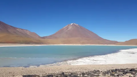 Marvel at the Beauty of the Laguna Verde | Ile Tours A stunning view of a turquoise lake with a majestic mountain in the background, under a clear blue sky. | Ile Tours