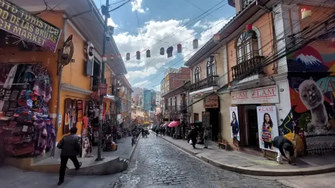 Explore the Lively Streets of La Paz | Ile Tours A vibrant street scene in La Paz, Bolivia, with colorful buildings, street vendors, and people walking, adorned with decorative lanterns. | Ile Tours