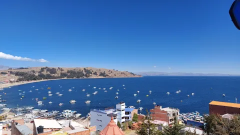Uma vista panorâmica do pitoresco Lago Titicaca das margens de Copacabana, Bolívia, com barcos na água e a bela paisagem sob um céu azul claro | Ile Tours