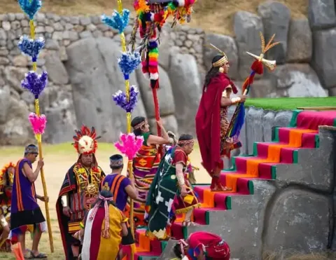 Participantes incas subindo escadas coloridas durante o Festival do Sol em Cusco, exibindo roupas tradicionais e decorações vibrantes | Ile Tours