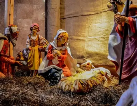 Una escena detallada de un nacimiento con figuras de María, José y los Tres Reyes Magos, con un fondo suavemente iluminado y paja esparcida alrededor | Ile Tours
