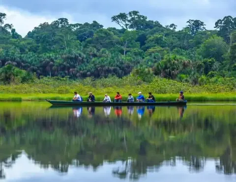 A group of travelers in a canoe gliding through the calm waters of the Amazon, surrounded by lush greenery and reflections on the water | Ile Tours