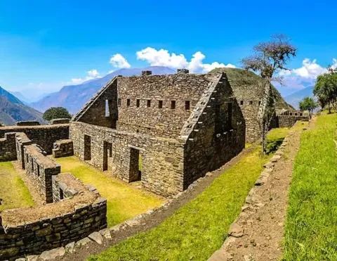 Stone ruins of an ancient Inca structure set against a vibrant blue sky and verdant mountains, showcasing the architectural beauty of Peru's historical legacy | Ile Tours