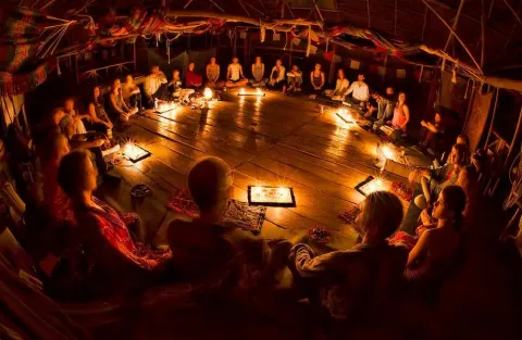Participantes en círculo alrededor de un fuego central en un espacio ceremonial poco iluminado, involucrados en un ritual comunitario | Ile Tours