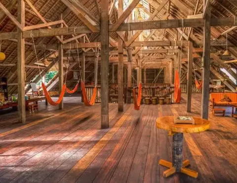 Un acogedor interior de una espaciosa estructura de madera con hamacas colgando y luz natural entrando, creando un ambiente cálido | Ile Tours