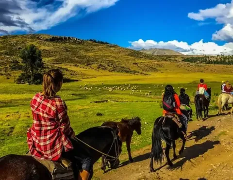 Grupo de viajeros montando a caballo por campos verdes en Cusco | Ile Tours