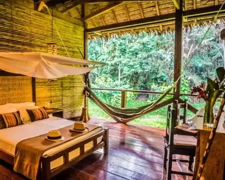 Una acogedora habitación de eco-alojamiento con una cama grande, una hamaca y vistas abiertas a la exuberante selva, creando un ambiente relajante | Ile Tours