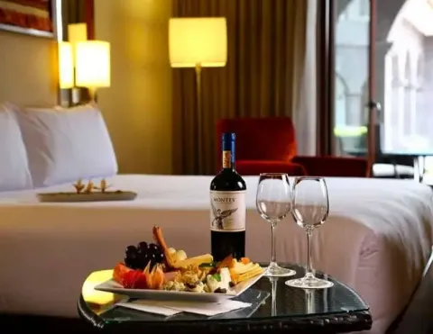 Una lujosa habitación de hotel con un plato bellamente dispuesto de frutas y bocadillos, acompañado de una botella de vino y dos copas, que transmite un ambiente acogedor y invitante | Ile Tours