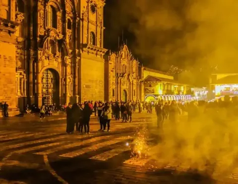 Una escena festiva en Cusco con personas celebrando la Noche de Año Nuevo entre humo y fuegos artificiales | Ile Tours