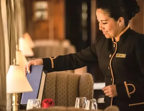 A smiling waitress setting a table in an elegant dining setting with soft lighting | Ile Tours