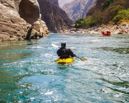 Um caiaqueiro remando por um rio sereno cercado por altas paredes de canyon e beleza natural | Ile Tours