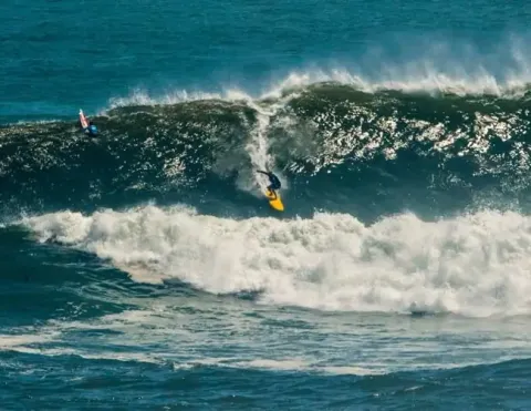 A surfer riding a massive wave at Punta Hermosa, Peru, showcasing the thrill of surfing against a backdrop of powerful ocean waves | Ile Tours