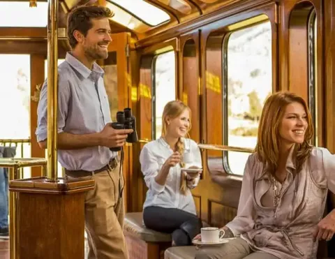 Huéspedes disfrutando de un viaje en tren panorámico, sonriendo y bebiendo mientras admiran la vista | Ile Tours