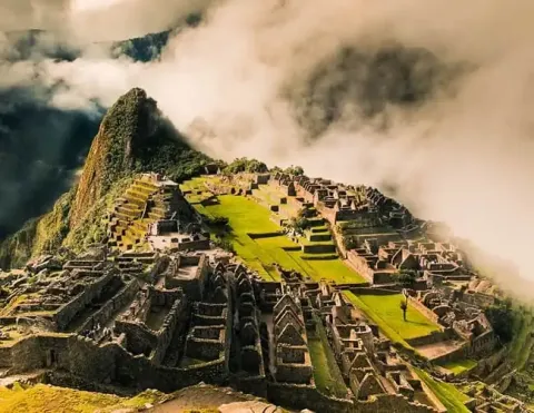 Una vista aérea de la majestuosa Machu Picchu, rodeada de nubes y montañas | Ile Tours
