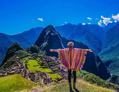 Viajera con poncho colorido mirando las ruinas de Machu Picchu | Ile Tours