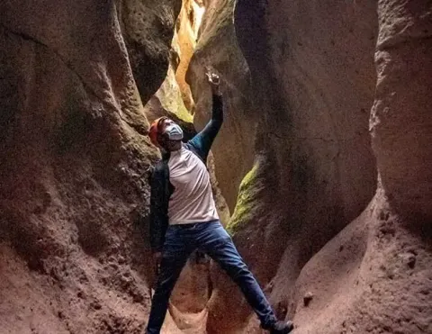 Explorer looking up inside the narrow rock walls of Qorihuillca Canyon | Ile Tours