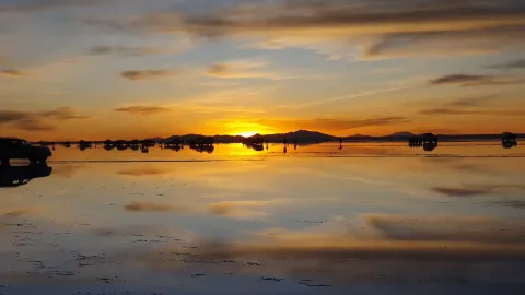 A stunning view of a person photographing a dancer in colorful attire on the reflective surface of the Salar de Uyuni, with distant mountains and clouds creating a breathtaking backdrop | Ile Tours