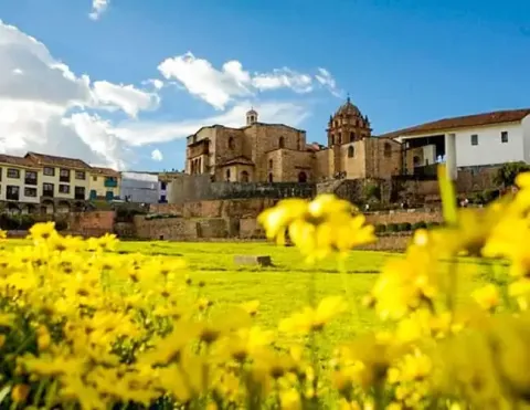 Uma bela vista de um edifício histórico em Cusco rodeado por flores amarelas vibrantes e um céu azul claro | Ile Tours
