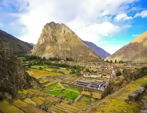 Vista panorâmica do Vale Sagrado no Peru, mostrando campos em terraços, uma aldeia aos pés de uma montanha e céus azuis impressionantes com nuvens | Ile Tours