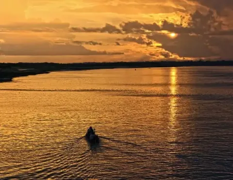 Un impresionante atardecer sobre un río tranquilo, con tonos dorados cálidos reflejándose en el agua y un pequeño bote deslizándose por la superficie | Ile Tours