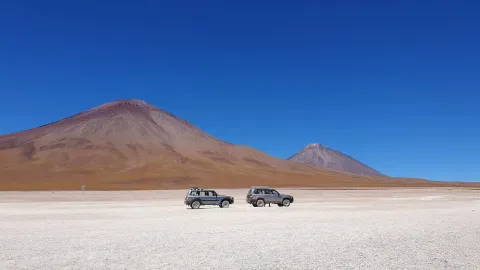 Two SUVs parked on a vast, arid landscape with mountains in the background under a clear blue sky, showcasing the stunning natural beauty of the region. | Ile Tours