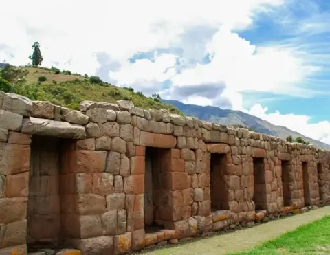 Close-up of ancient stone walls with openings, set against a backdrop of rolling hills and a blue sky, representing the architectural heritage of the Inca civilization | Ile Tours