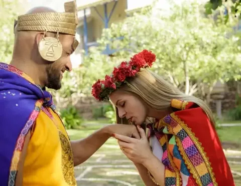 Pareja en vestimenta tradicional andina, con la mujer besando suavemente la mano del hombre, rodeados de un jardín vibrante | Ile Tours