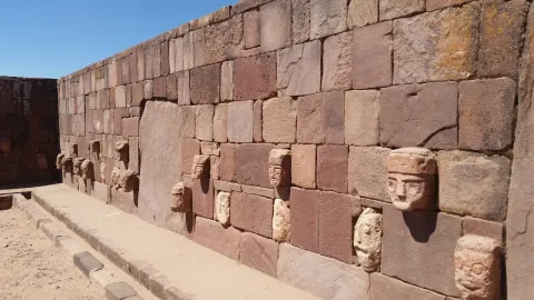 A antiga parede de pedra de Tiwanaku, com cabeças esculpidas em pedra, mostrando a notável arquitetura e história deste sítio arqueológico pré-colombiano na Bolívia | Ile Tours