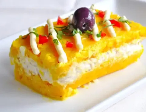 A beautifully plated Causa Limeña, a traditional Peruvian layered potato dish, garnished with fresh avocado, black olives, and a slice of boiled egg, showcasing the vibrant flavors of Peru | Ile Tours