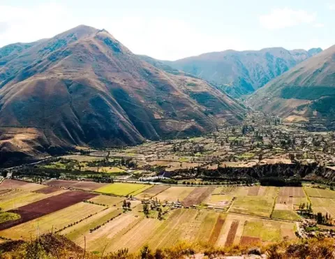 Uma artesã local demonstra técnicas tradicionais de tecelagem em um mercado colorido no Vale Sagrado, Peru, cercada por tecidos e fios vibrantes, mostrando a rica herança cultural da região | Ile Tours