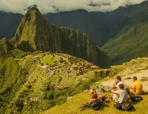 Tourists sitting on a ledge admiring the breathtaking view of Machu Picchu and the surrounding mountains | Ile Tours