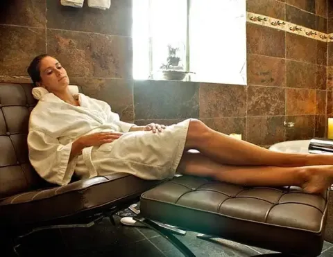 Mujer relajándose en una tumbona en un spa vistiendo una bata blanca | Ile Tours