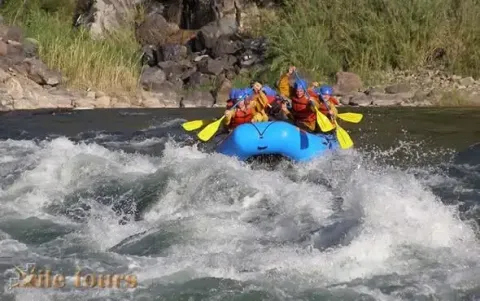 Um grupo de rafters navegando alegremente por corredeiras em uma balsa azul brilhante | Ile Tours